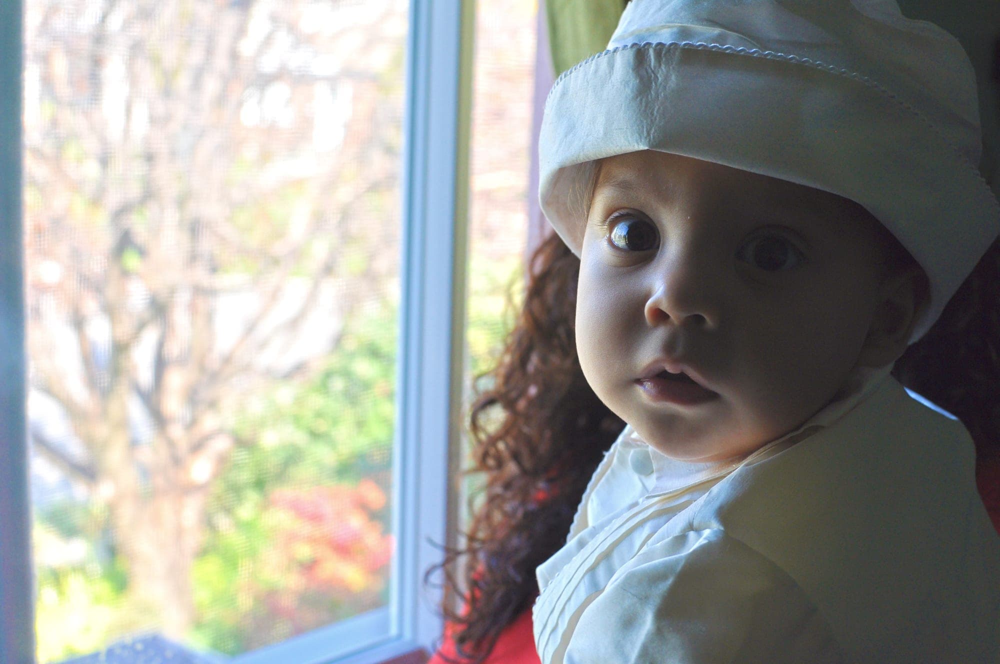 Child in a white christening cap lit by a bright window
