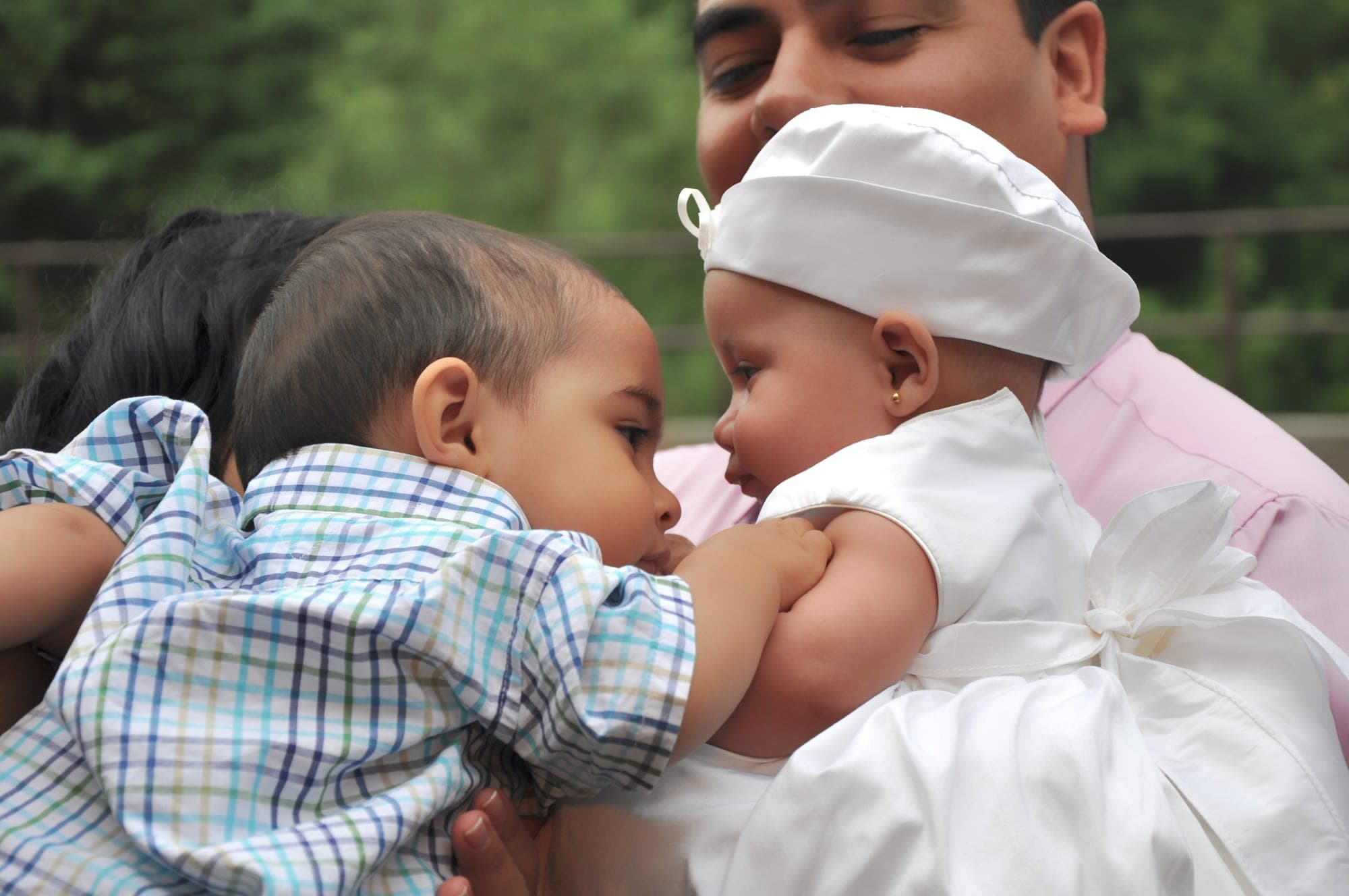 Two babies in white christening outfits held together