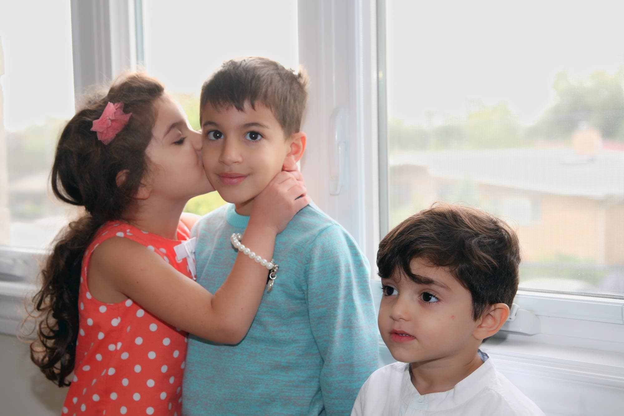 Two children sharing a kiss in soft window light