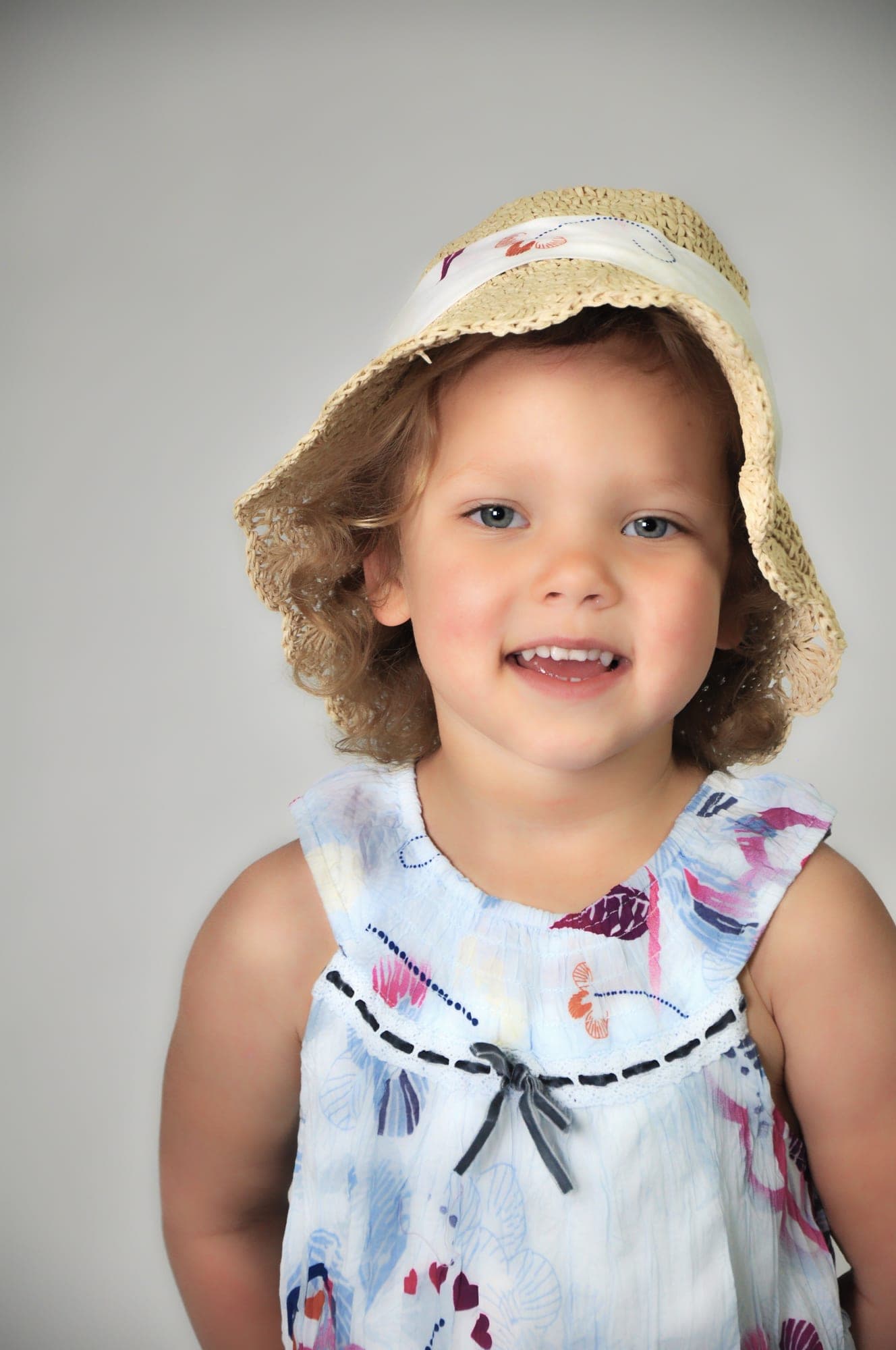 Young girl in a blue floral dress and straw hat, studio portrait