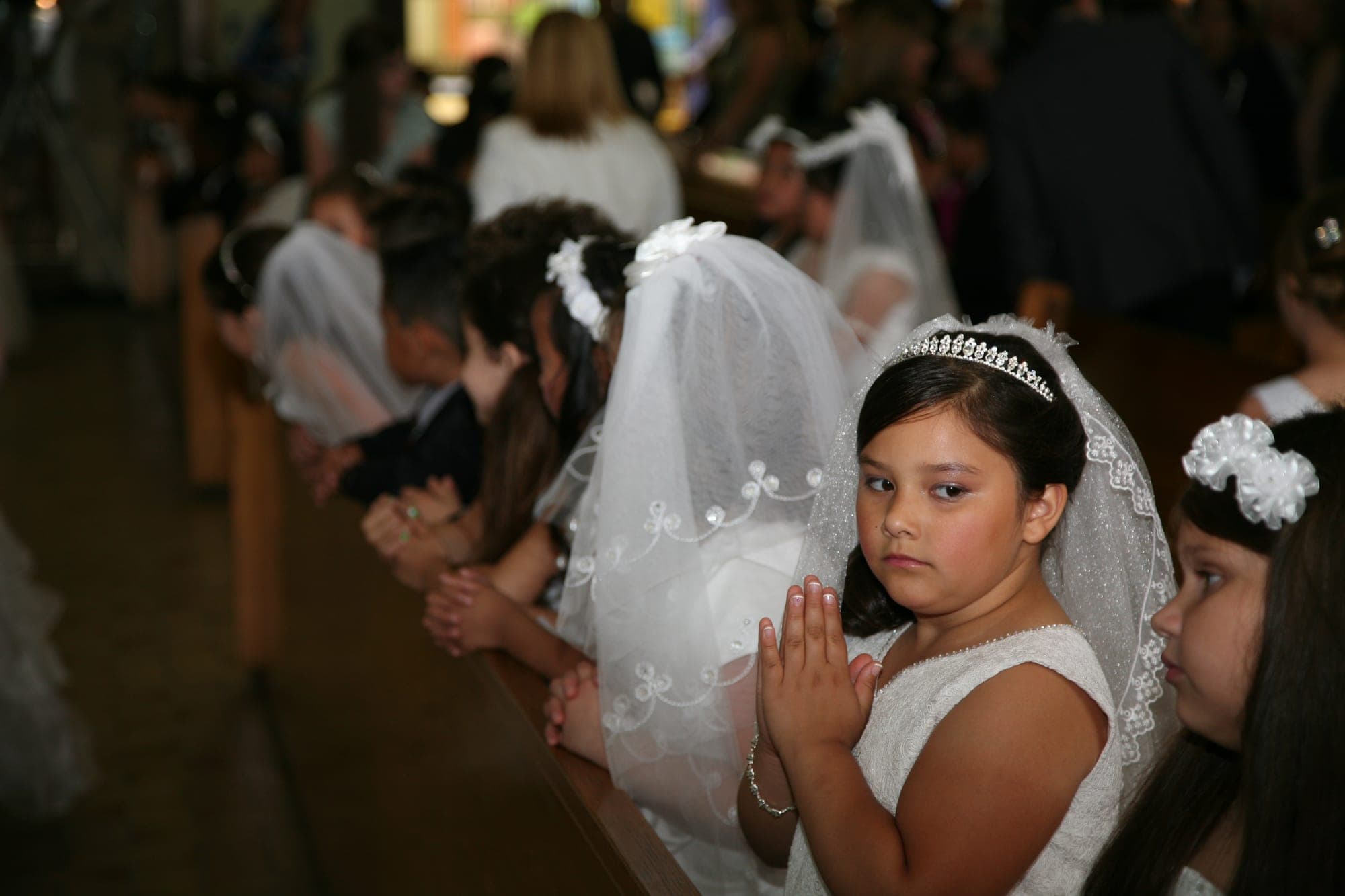 Girls in communion veils praying in the church pews
