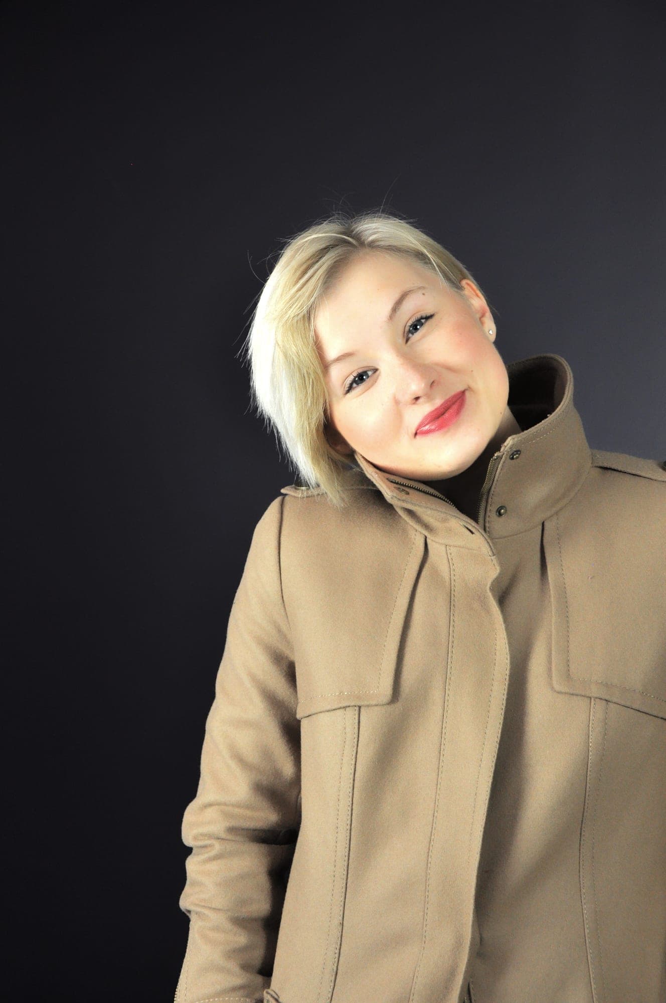 Smiling headshot of a woman in a tan coat against a dark backdrop