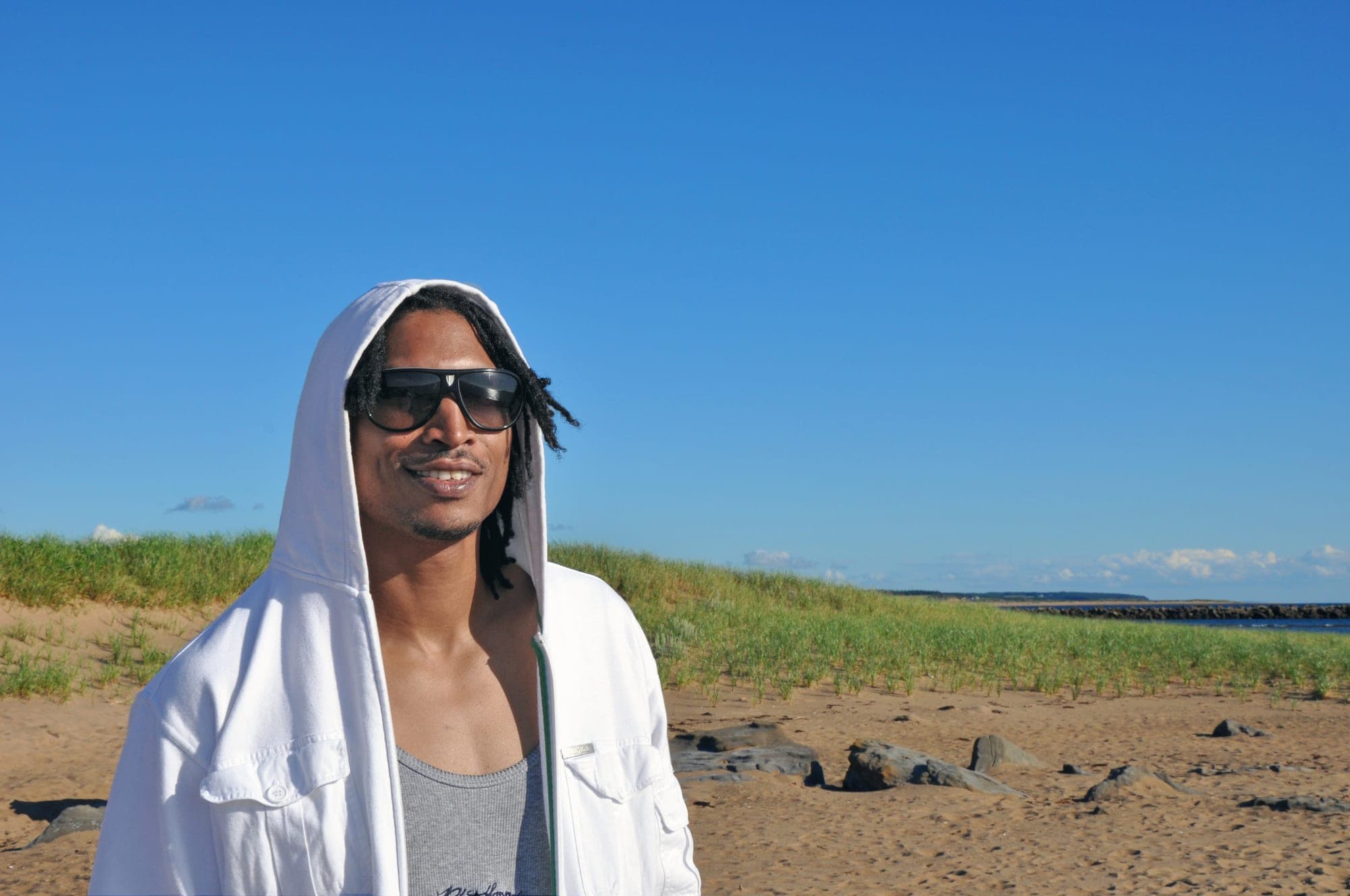 Portrait of a man in a white hoodie and sunglasses on a beach