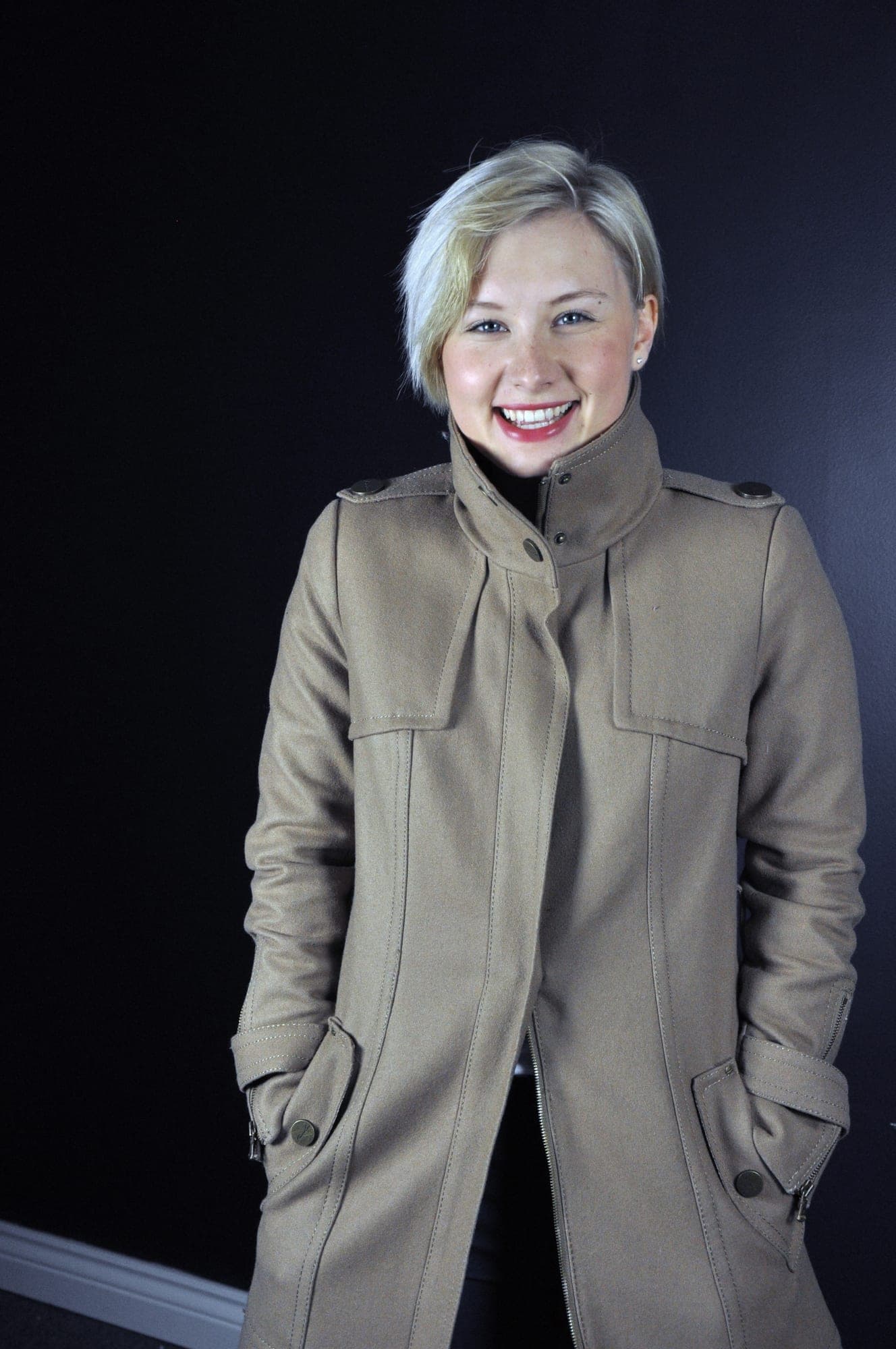 Portrait of a woman in a tan trench coat against a dark backdrop