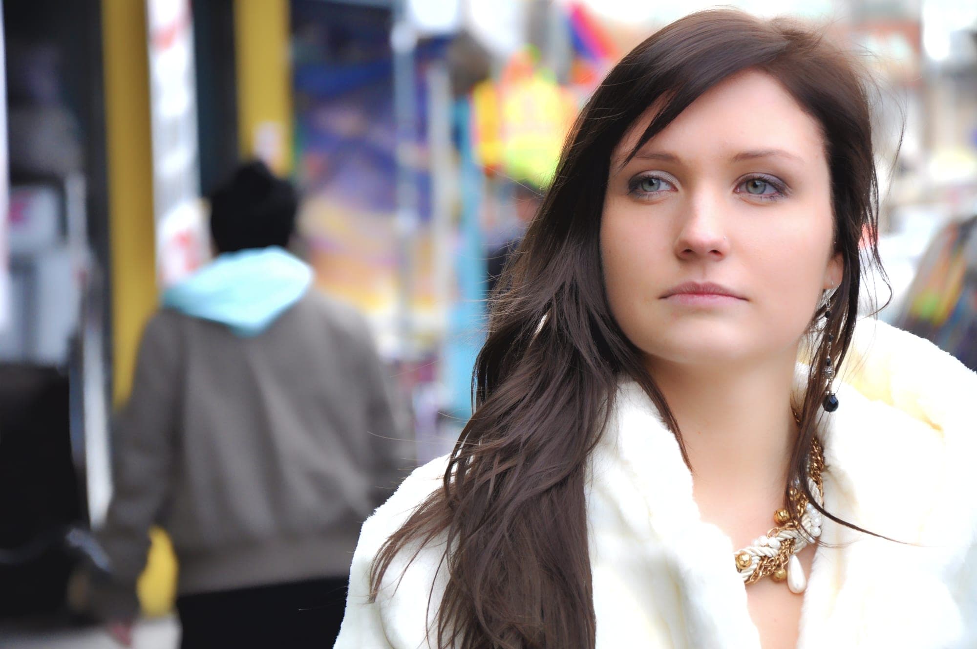 Street portrait of a woman in a white coat with city bokeh behind