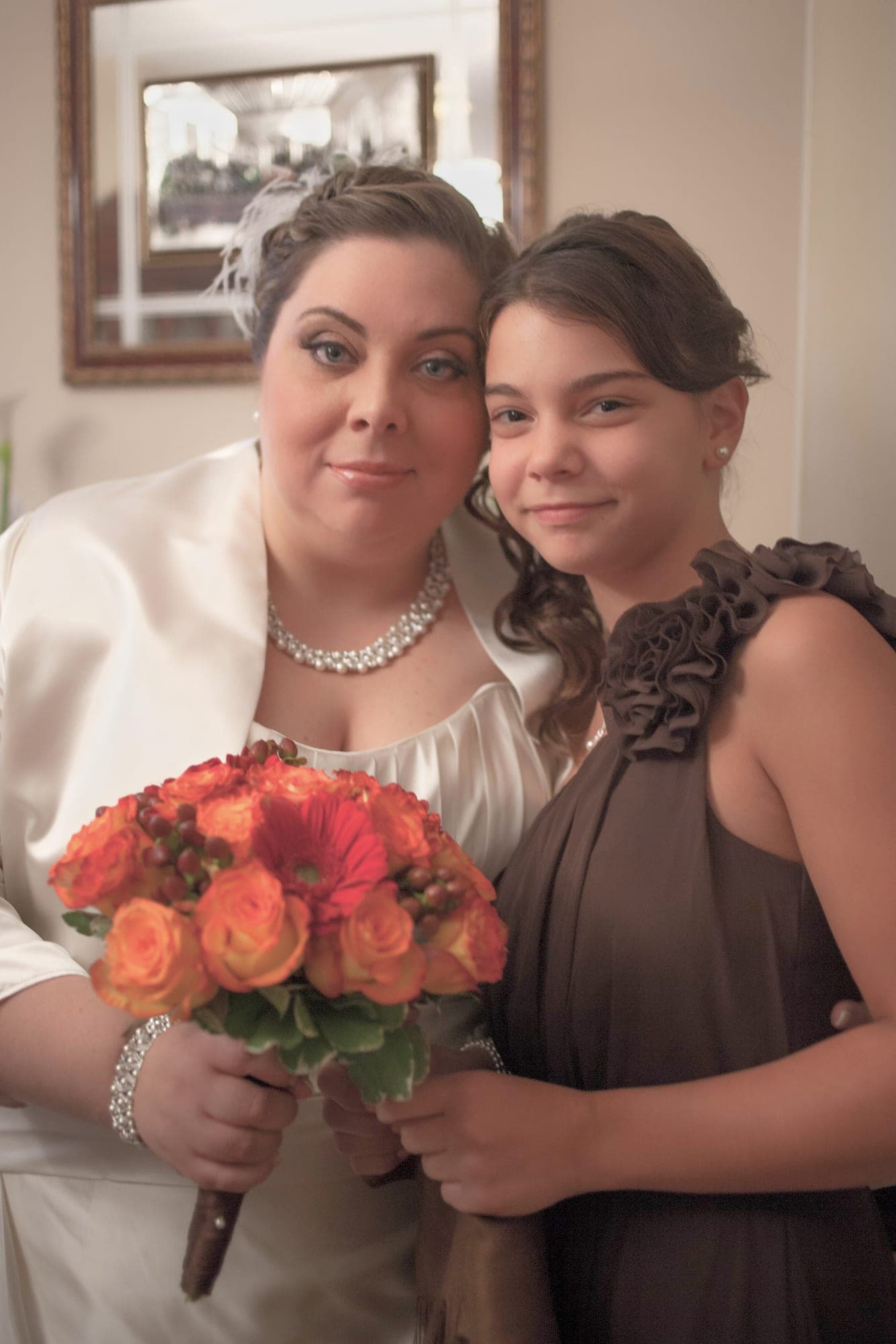 Bride holding an orange rose bouquet beside her junior bridesmaid