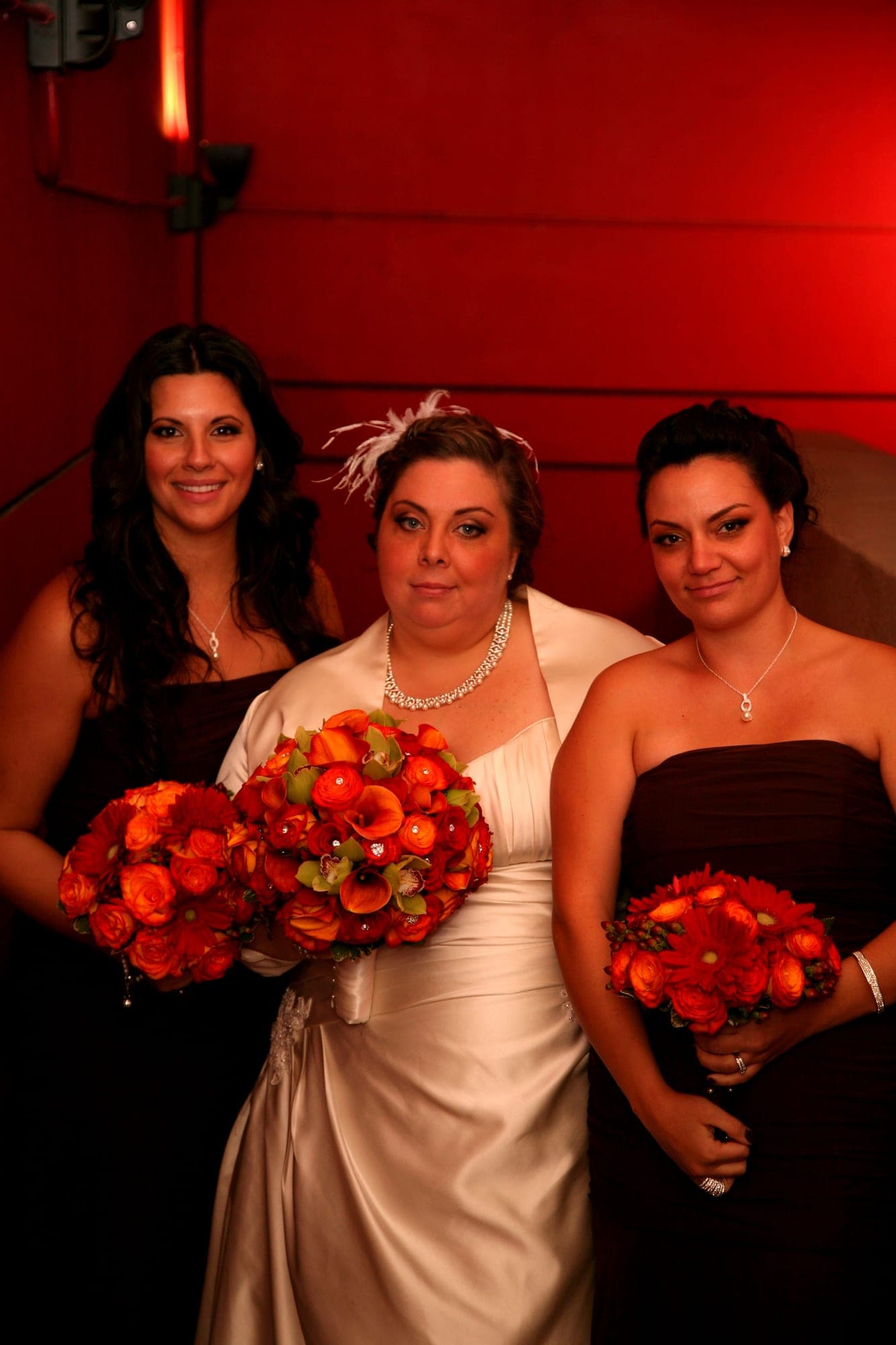 Bridesmaids holding red rose bouquets under warm uplighting