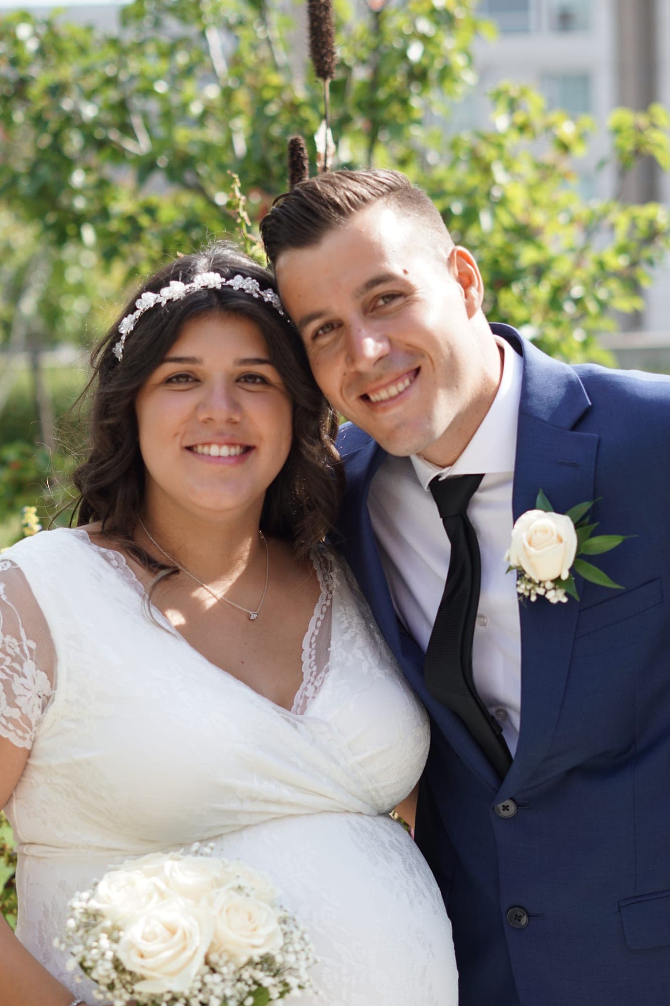 Bride and groom embracing in front of summer greenery