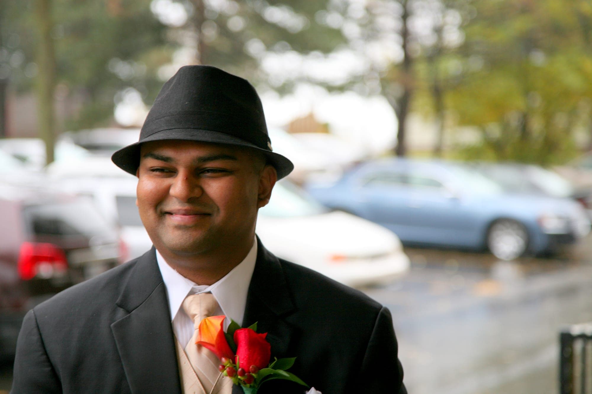 Groom in a fedora wearing an orange rose boutonniere