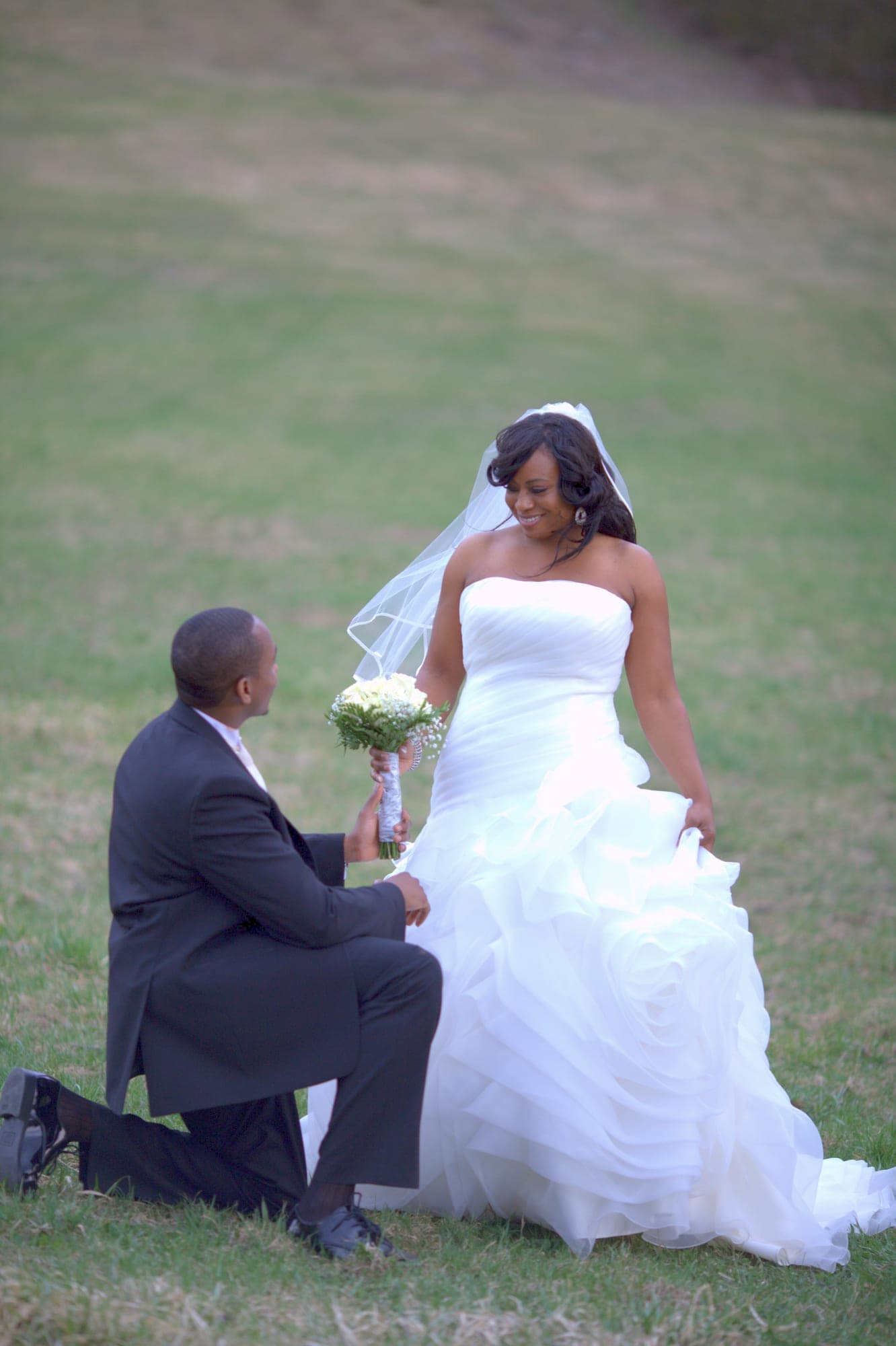Groom kneeling to his bride on a sunlit lawn