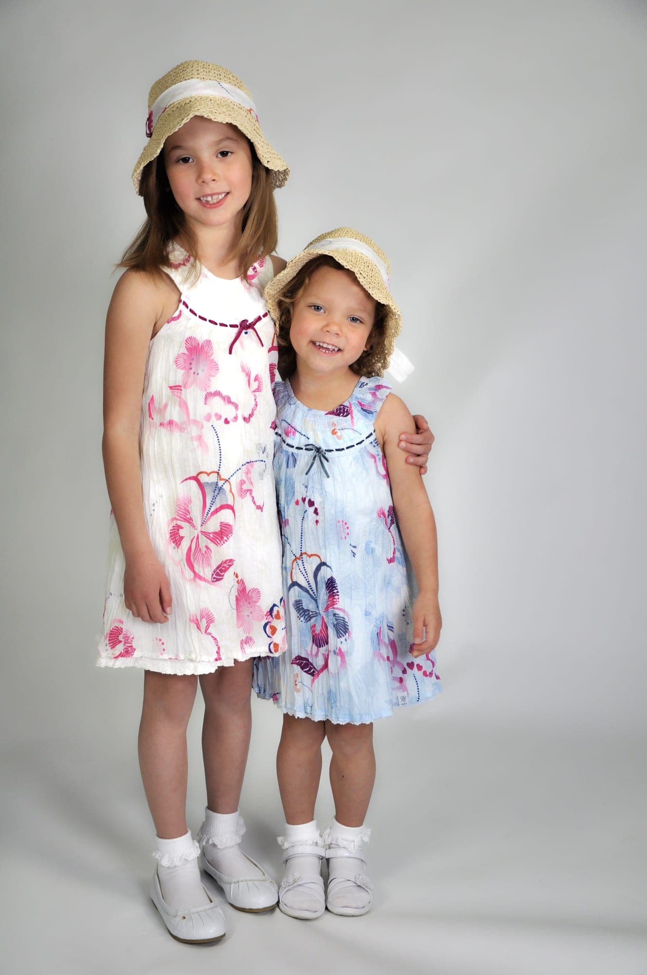Two sisters in matching floral dresses and straw hats