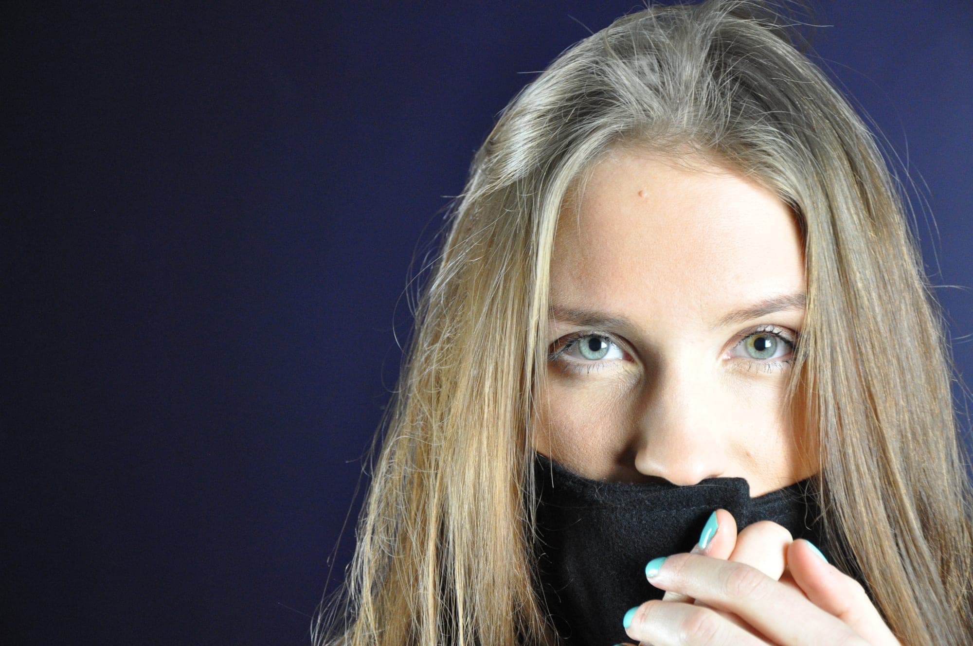 Portrait of a woman pulling a turtleneck over her mouth, blue backdrop