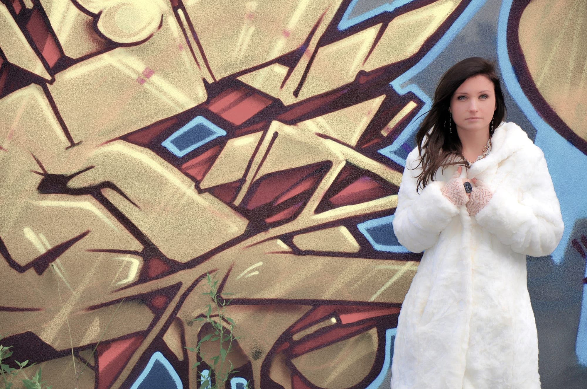 Editorial portrait of a woman in a white coat against a graffiti wall