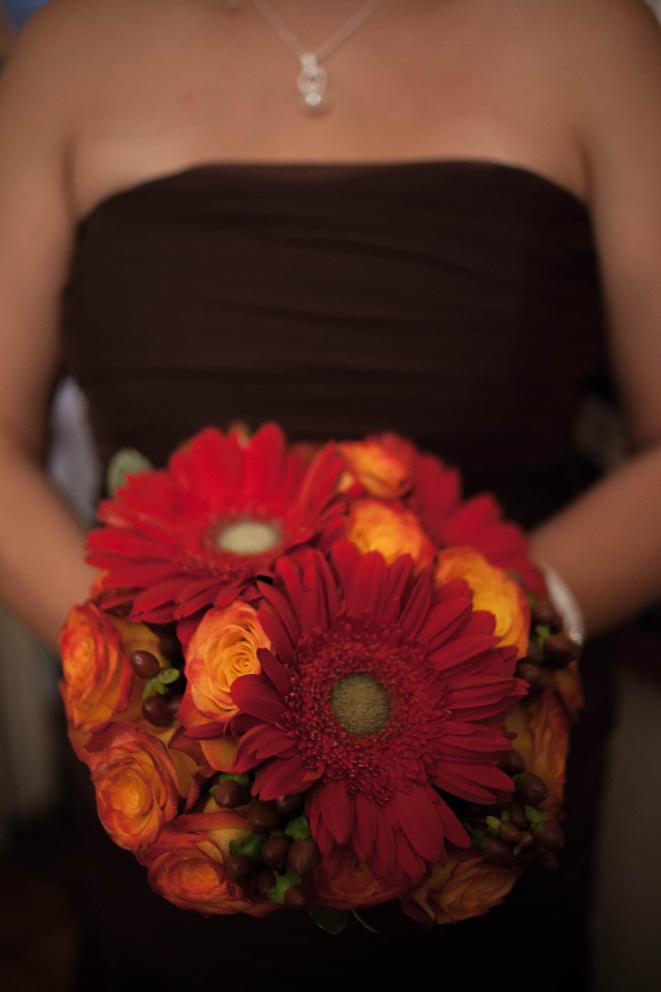 Red gerbera and orange rose bouquet against a chocolate bridesmaid dress